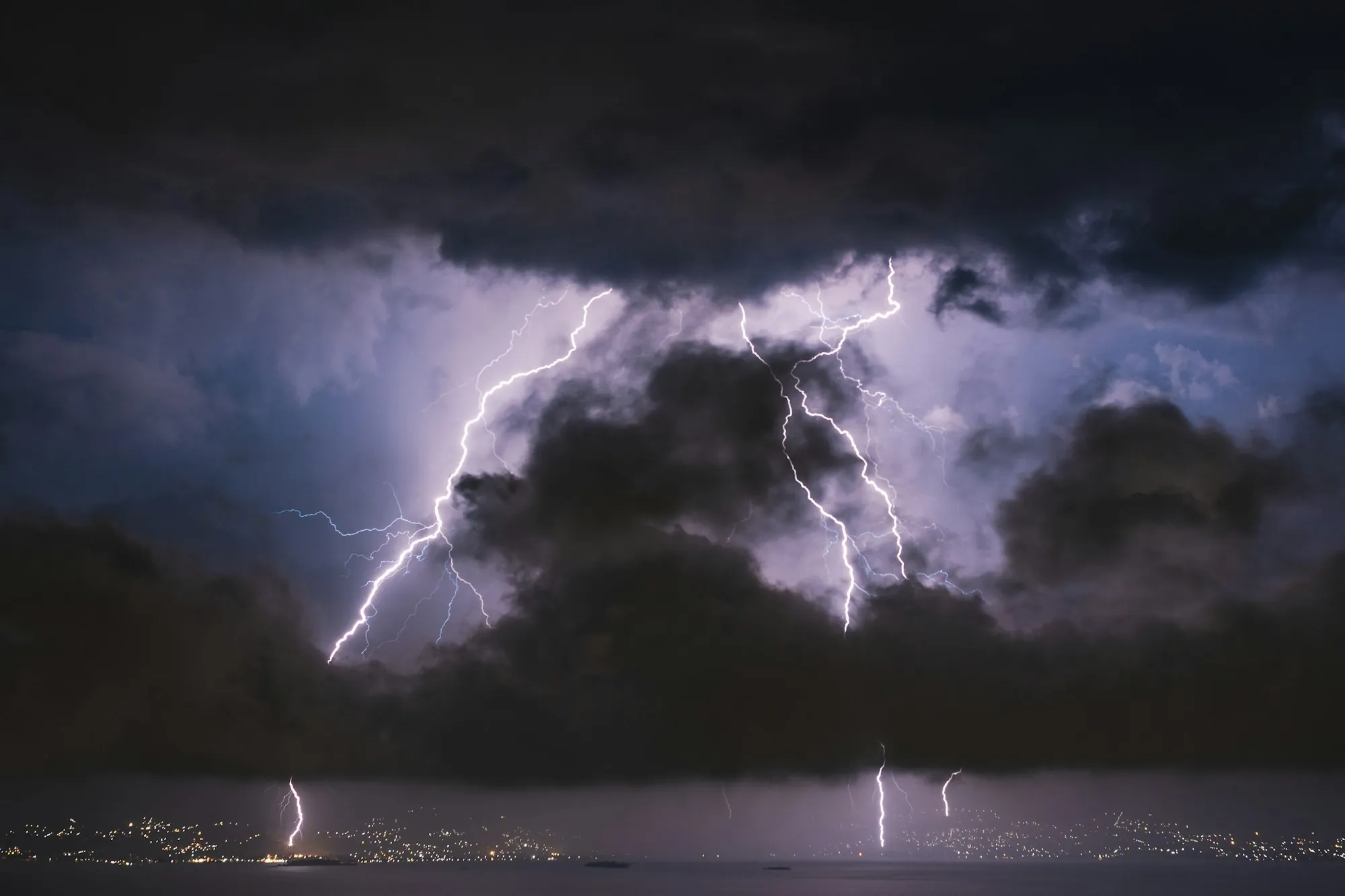 Lightning over a dark sky above a hillside town at night